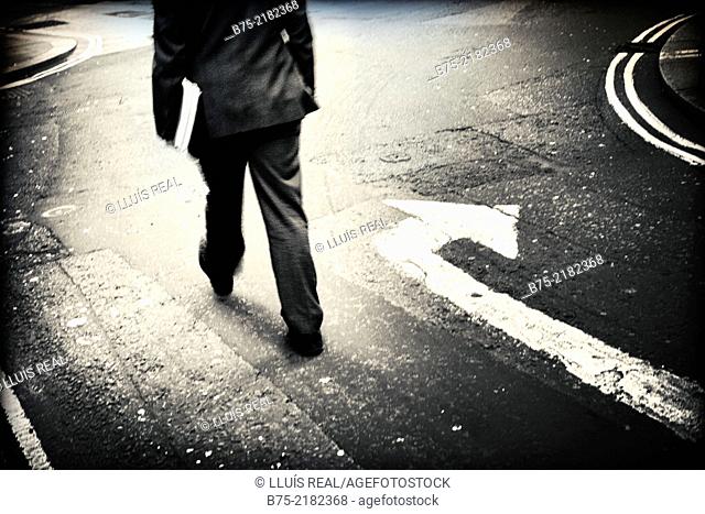 Legs of unrecognizable businessman with portfolio walking down in the street with a turn arrow painted on the asphalt in the city of London, England, UK