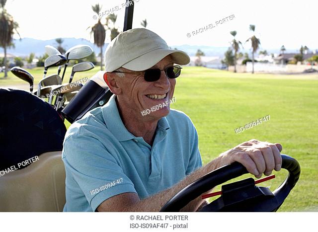 Senior male golfer driving golf buggy