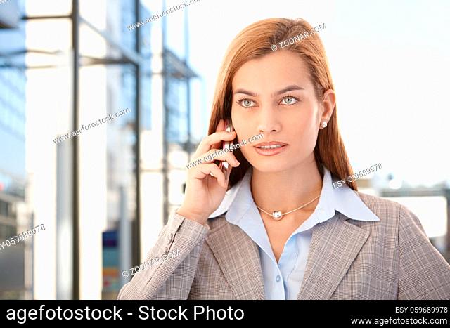 Beautiful young businesswoman talking on mobile phone in business quarter