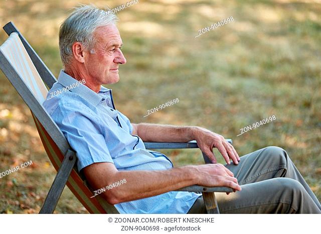 Alter Mann sitzt entspannt im Liegestuhl im Sommer in der Natur