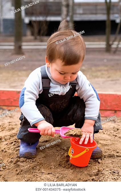 Child sitting in sandbox making mud pie