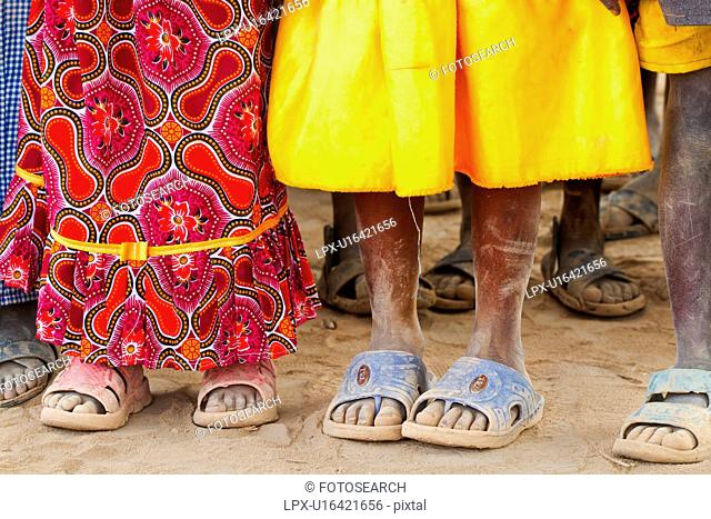 Close up detail of Masai children's feet, all wearing dusty sandals, and brightly coloured clothing, Amboseli, Kenya, East Africa