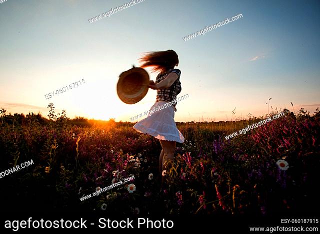 Back view woman in white skirt running in summer meadow holding straw hat in hand. Depersonalization concept. Playful girl feeling free in natural environment