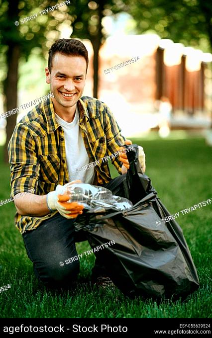 Young man collects garbage in a bag in park, volunteering. Male person cleans forest, ecological restoration, eco lifestyle, trash collection and recycling
