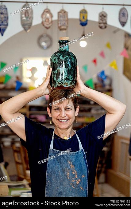Smiling artist carrying turquoise bottle on head at ceramic store