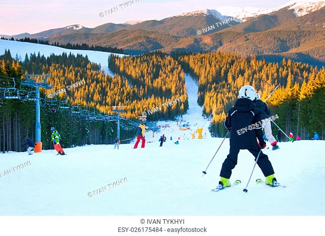 Skier and snowboarders on a mountains slope at sunset