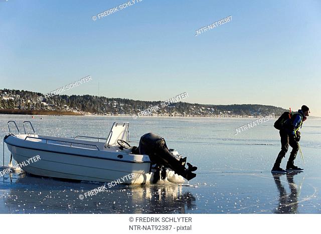 Man ice-skating near shore with moored motorboat
