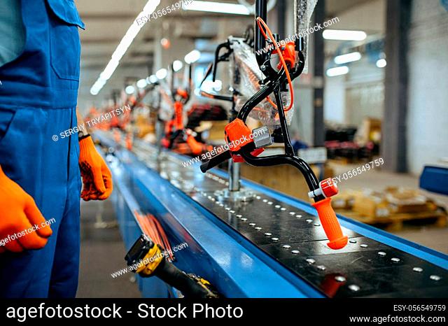 Bicycle factory, worker checks bike assembly line. Male mechanic in uniform installs cycle parts in workshop, industrial manufacturing