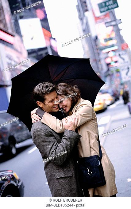 Couple huddled under umbrella on city street