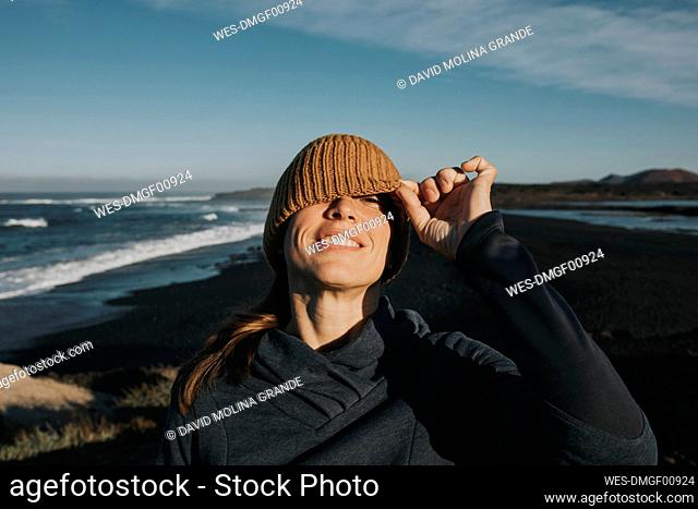 Smiling woman peeking through knit hat at Janubio Beach, Lanzarote, Canary Islands, Spain