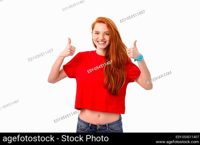 Happy young caucasian female making thumb up sign and smiling cheerfully, showing her support and respect to someone