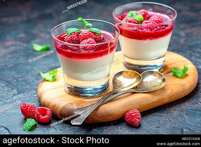 Glass cups with vanilla Panna cotta, fresh raspberries and mint leaves on wooden serving board, selective focus