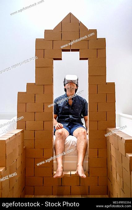 Man watching movie through virtual reality simulator seen through cardboard structure at home