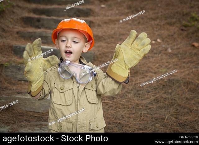 Happy adorable child boy with big gloves, hard hat and goggles playing handyman outside