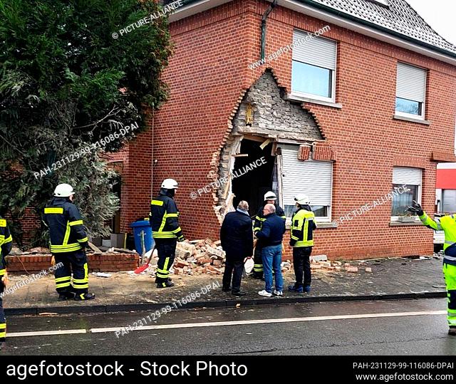 29 November 2023, North Rhine-Westphalia, Emsdetten: Emergency services stand in front of a large hole in the wall of a house caused by a truck