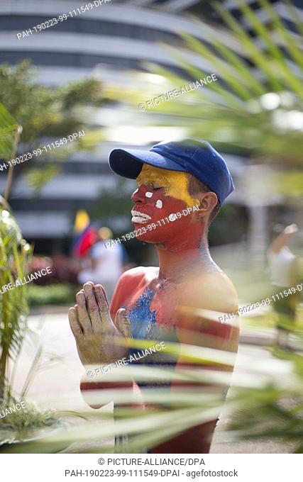 23 February 2019, Venezuela, Caracas: A man wearing Venezuelan make-up prays for humanitarian aid in the capital during a rally