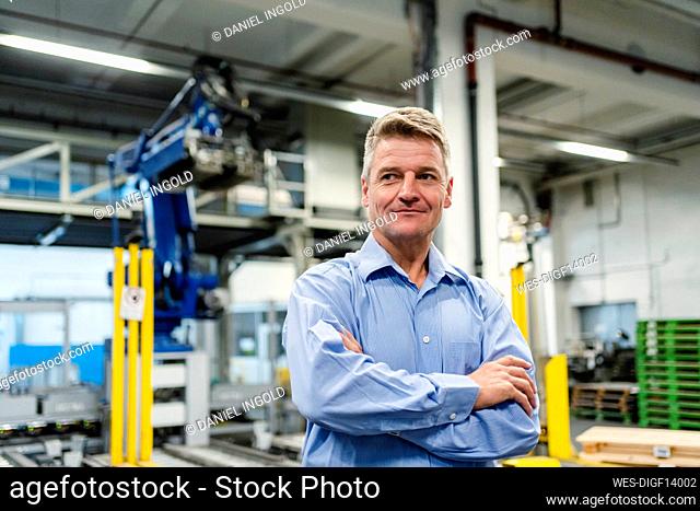 Smiling supervisor with arms crossed looking away in industry