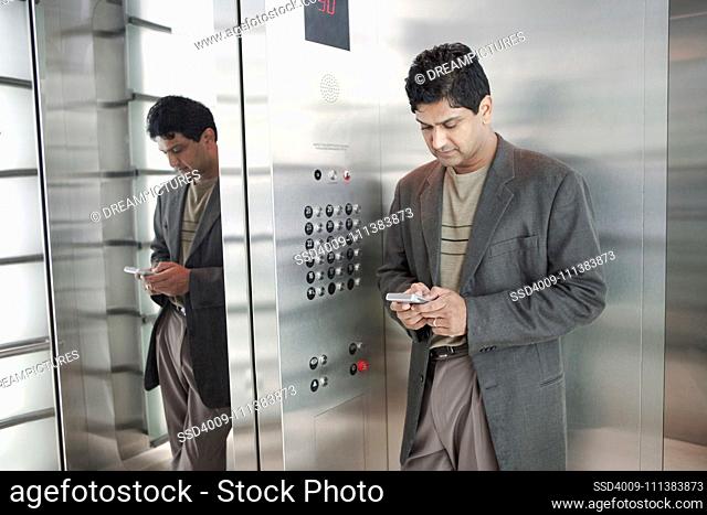 Indian businessman text messaging on cell phone in elevator