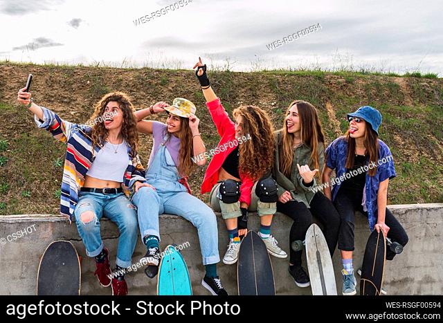 Happy female friends taking selfie through mobile phone on retaining wall