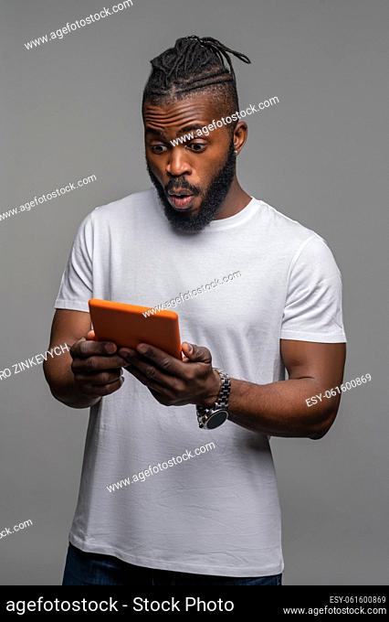 Dazed focused muscular cute young African American man watching a video on the tablet computer