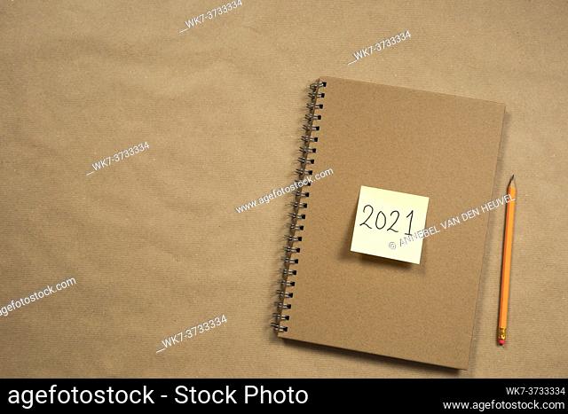 Top view of Brown notepad and yellow sticky note with 2021 New Year's message, pencil on brown paper background texture, education or business concept copy...
