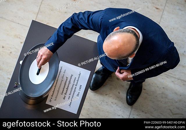 03 June 2022, Berlin: Chancellor Olaf Scholz (SPD) throws in his voting card in the Bundestag for the final vote on the amendment to the Basic Law on the...