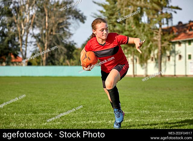 Girl with rugby ball running on sports field
