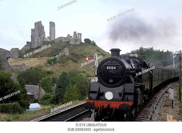 Corfe Castle seen behind a railway line with a steam train approaching