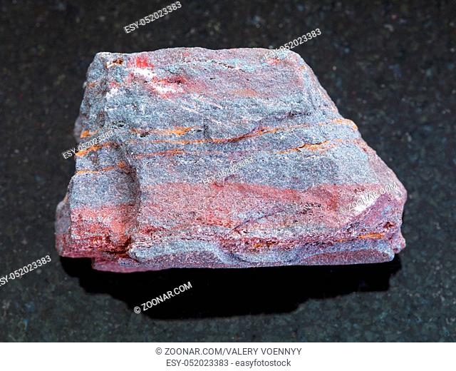 macro shooting of natural mineral rock specimen - rough jaspilite (ferruginous quartzite) stone on dark granite background