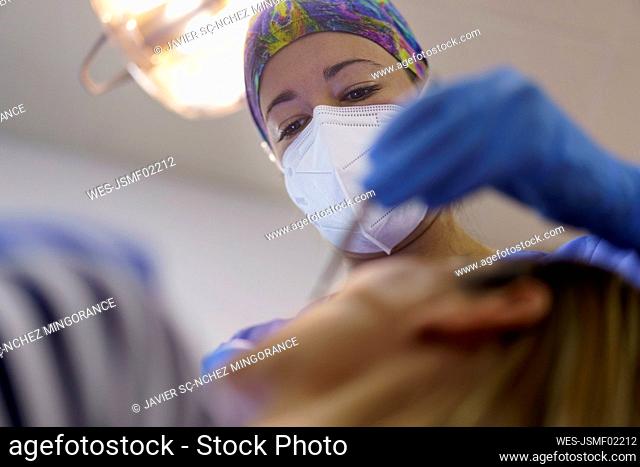 Female dentist wearing protective face mask examining patient's teeth at clinic