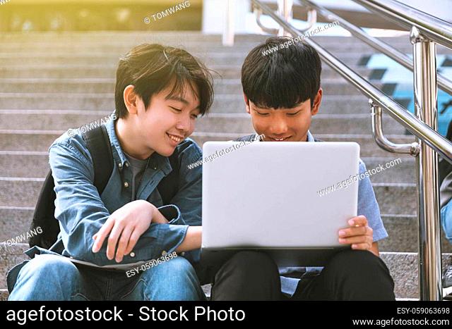 Happy teenager students looking at laptop and sitting on the stairs