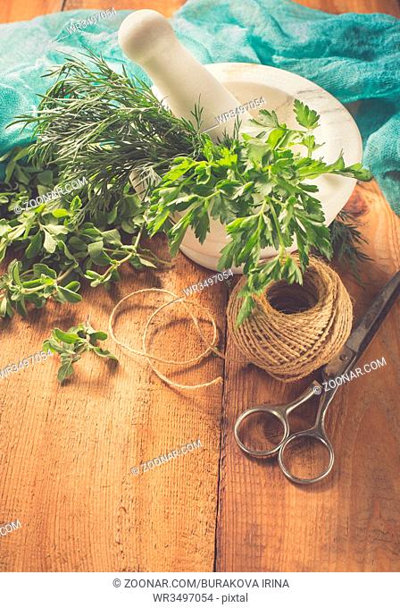 Spicy grass marjoram, dill, parsley, scissors and marble mortar on a wooden table. Retro style filter