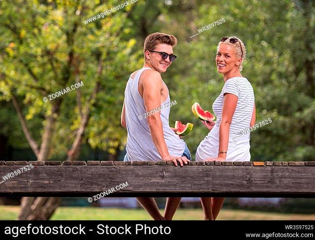 couple in love enjoying watermelon while sitting on the wooden bridge over the river in beautiful nature
