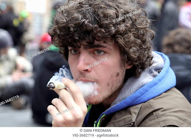 Young man smokes a large marijuana joint during the 420 Smoke Out at Yonge-Dundas Square in Toronto, Ontario, Canada. Several hundred cannabis smokers and...