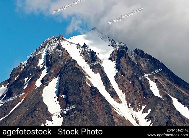 Mountainous landscape of Kamchatka Peninsula: view of top of rocky cone of Vilyuchinsky Volcano, mountain peak and steep slope of volcano with snowfield