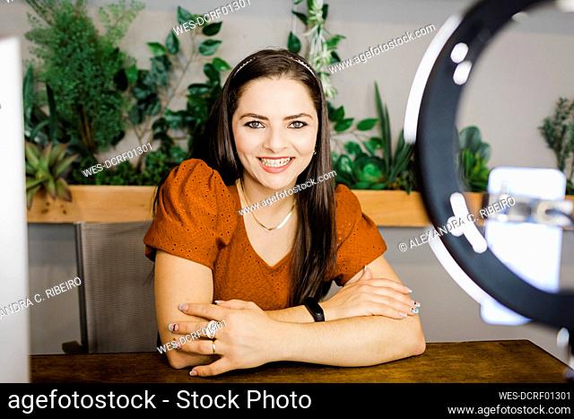 Happy young businesswoman sitting with arms crossed in office