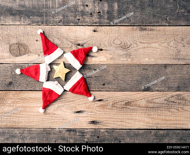 Star shape of hats of Santa with a golden star on a rustic wooden plank with space for text or image