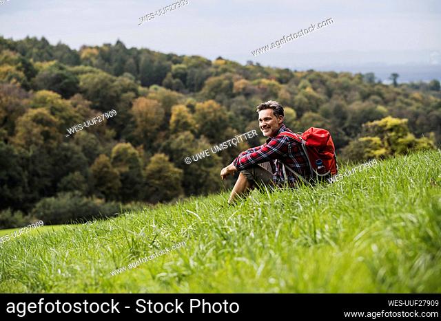 Smiling man with backpack sitting on grass