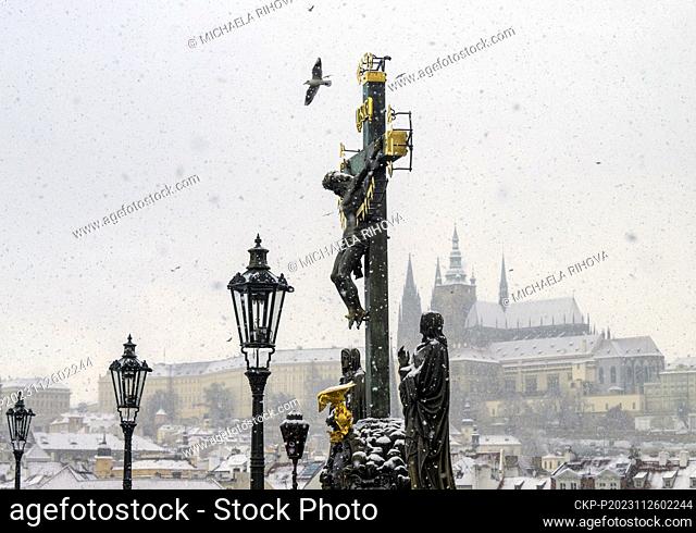 Snow-covered sculpture of the Holy Cross with Calvary on Charles Bridge in Prague, Czech Republic, on November 26, 2023. On the background is seen the Prague...
