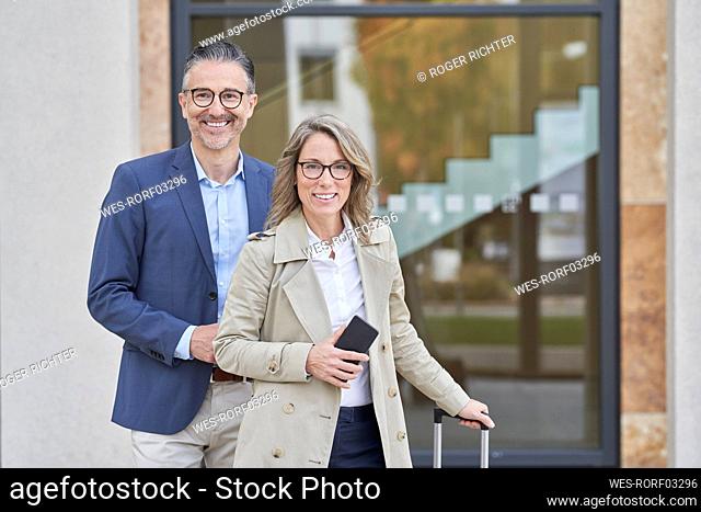 Happy business colleagues with luggage standing together in front of building