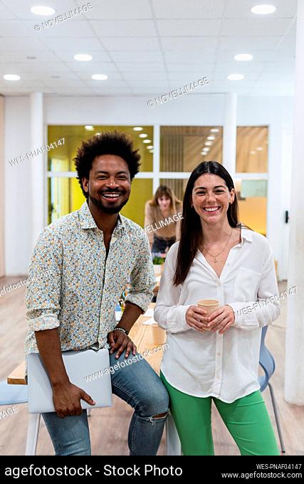 Portrait of happy businesswoman and businessman in office with colleagues in background