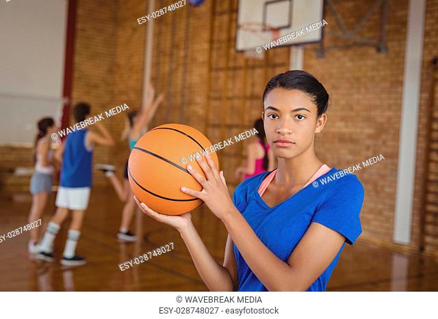 High school girl holding a basketball while team playing in background