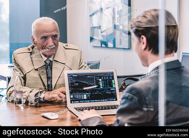 Young financial advisor sitting in front of laptop, consulting senior client with his investment strategy