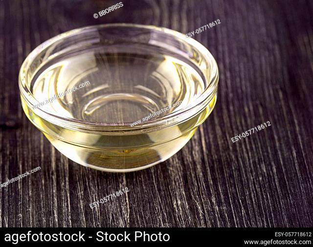 Cooking vegetable oil in a small glass cup on old wooden table