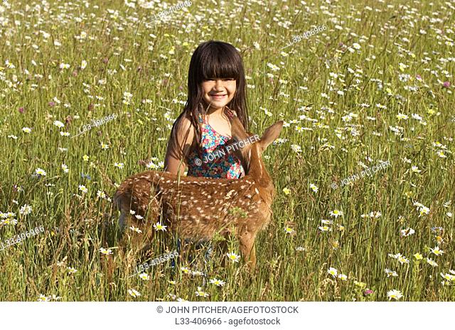 Girl with white tailed deer fawn in field of summer flowers