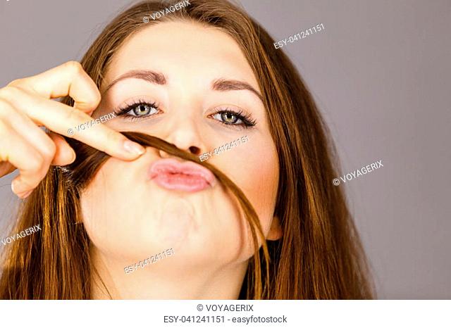 Woman having fun with her long brown hair making moustache being happy about hairdo condition, studio shot grey background