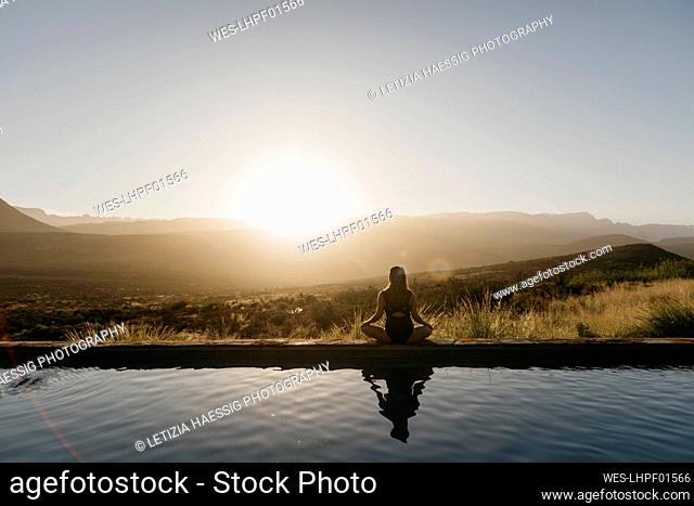 Woman doing yoga sitting by pool at sunset