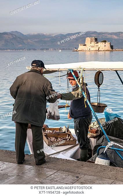 Selling fish from a fishing boat in the harbour at Nafplio with the Bourtzi island and fort in the background, Argolid, Peloponnese, Greece