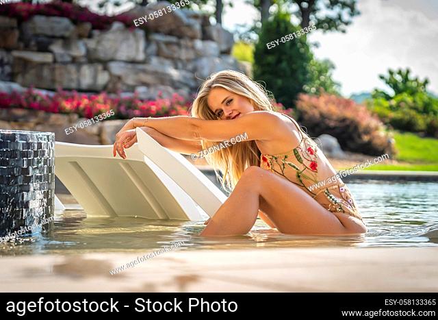 A gorgeous blonde bikini model enjoys a summers day by the pool