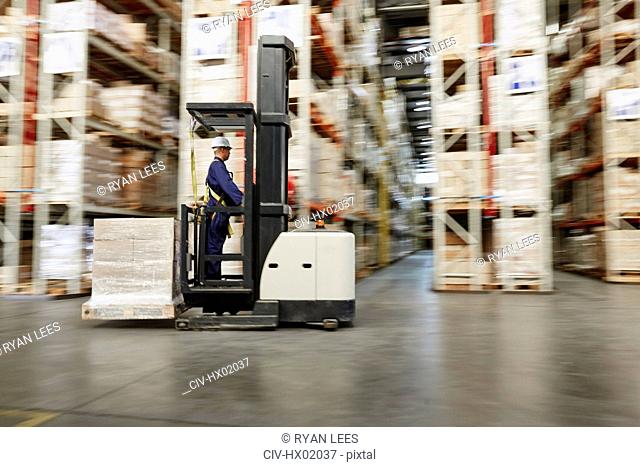 Worker operating forklift moving pallet of boxes in distribution warehouse